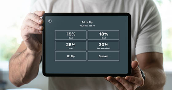 Man,Holding,A,Tablet,With,Tipping,Screen,Inside,A,Restaurant Man holding a tablet with tipping screen inside a restaurant